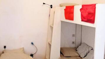 A small, compact room with bunk beds, a single bed, and a white wall.