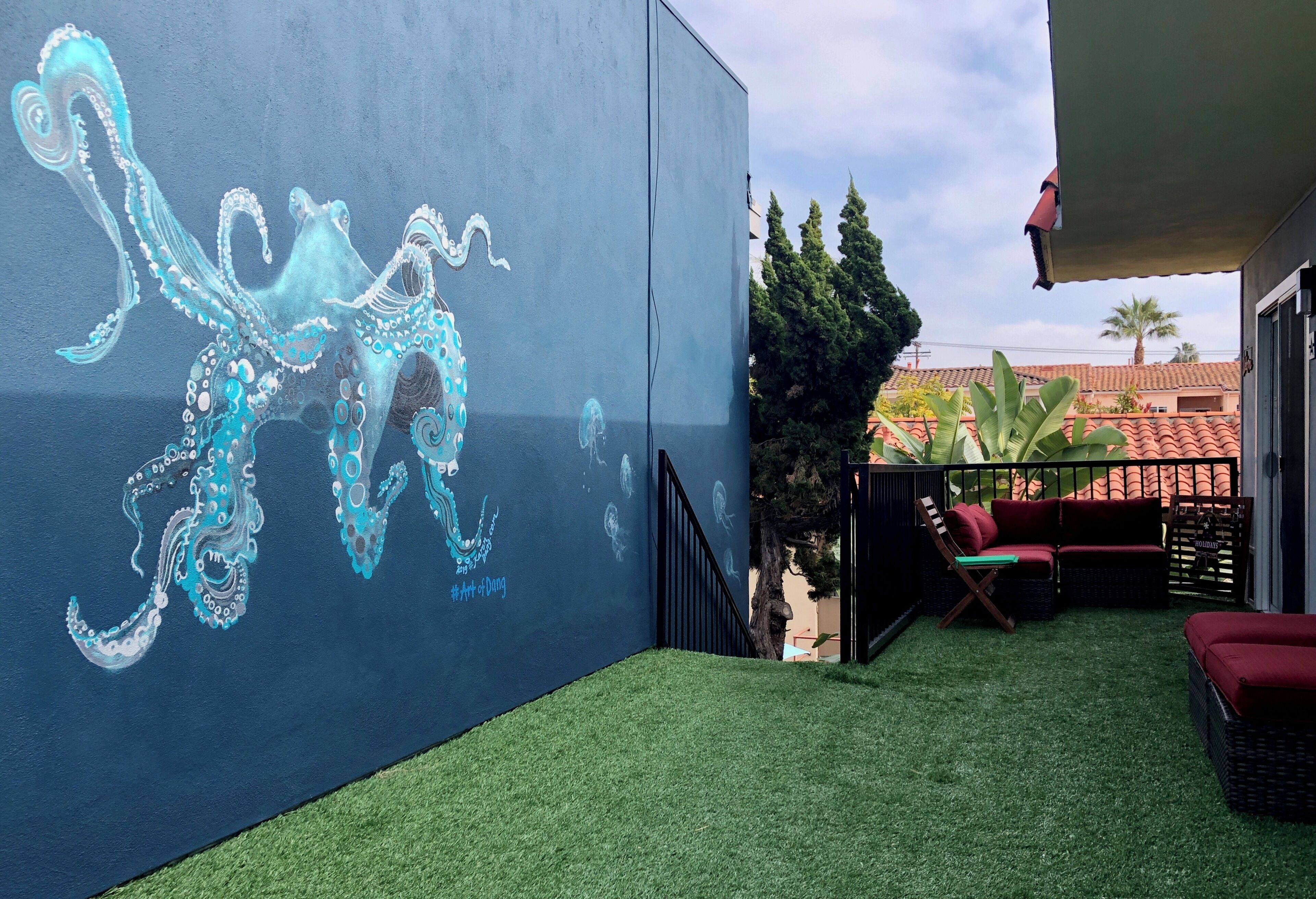 Un balcón con césped artificial, un sofá rojo y un mural de un pulpo.