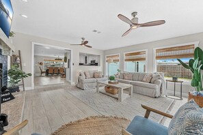 A spacious living room with a fireplace, a ceiling fan, and a view of the backyard.