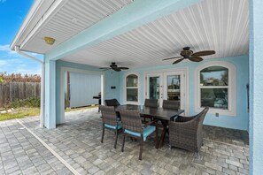 An outdoor patio with a table and chairs, a ceiling fan, and a view of the backyard.