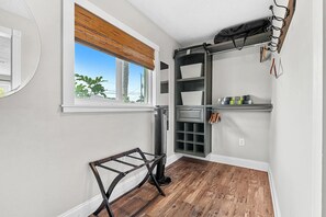 A room with a window, a radiator, a shelf with storage boxes, and a rack with hanging items.
