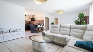 En moderne stue med en hjørnesofa, et glasbord og et køkken i baggrunden.