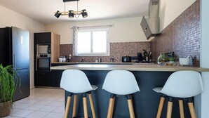 Et moderne køkken med en central ø, barstole, et køleskab og et vindue.