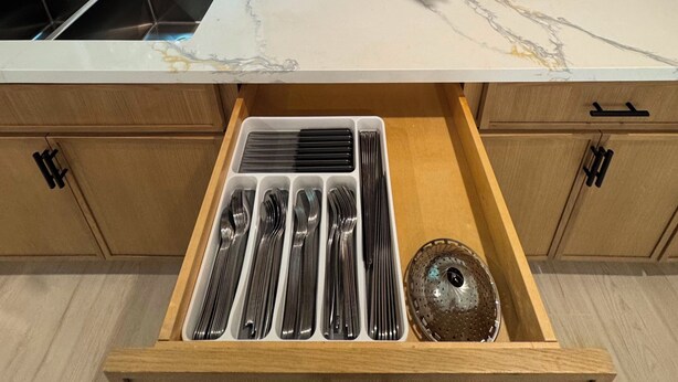 Cozinha com bancada de mármore, pia embutida e organizador de gaveta com utensílios.