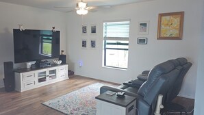 A living room with a flat-screen TV, a sofa, a coffee table, and a rug. - 3-bedroom house in peaceful Fort Myers near Lehigh Acres with AC comfort (Fort Myers)