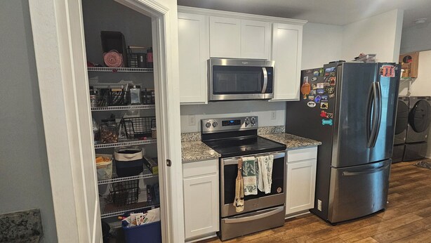 A kitchen with white cabinets, a stainless steel refrigerator, a microwave, an oven, and a built-in dishwasher. - 3-bedroom house in peaceful Fort Myers near Lehigh Acres with AC comfort (Fort Myers)