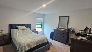 A bedroom with a bed, dresser, nightstand, and a window. - 3-bedroom house in peaceful Fort Myers near Lehigh Acres with AC comfort (Fort Myers)
