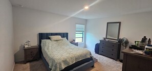 Ein Schlafzimmer mit Bett, Kommode, Nachttisch und einem Fenster.