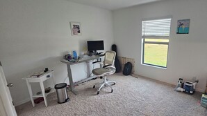 A room with a desk, chair, computer, and a window with a view of a field. - 3-bedroom house in peaceful Fort Myers near Lehigh Acres with AC comfort (Fort Myers)