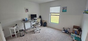 Ein Zimmer mit Schreibtisch, Stuhl, Computer und Fenster mit Blick auf ein Feld.