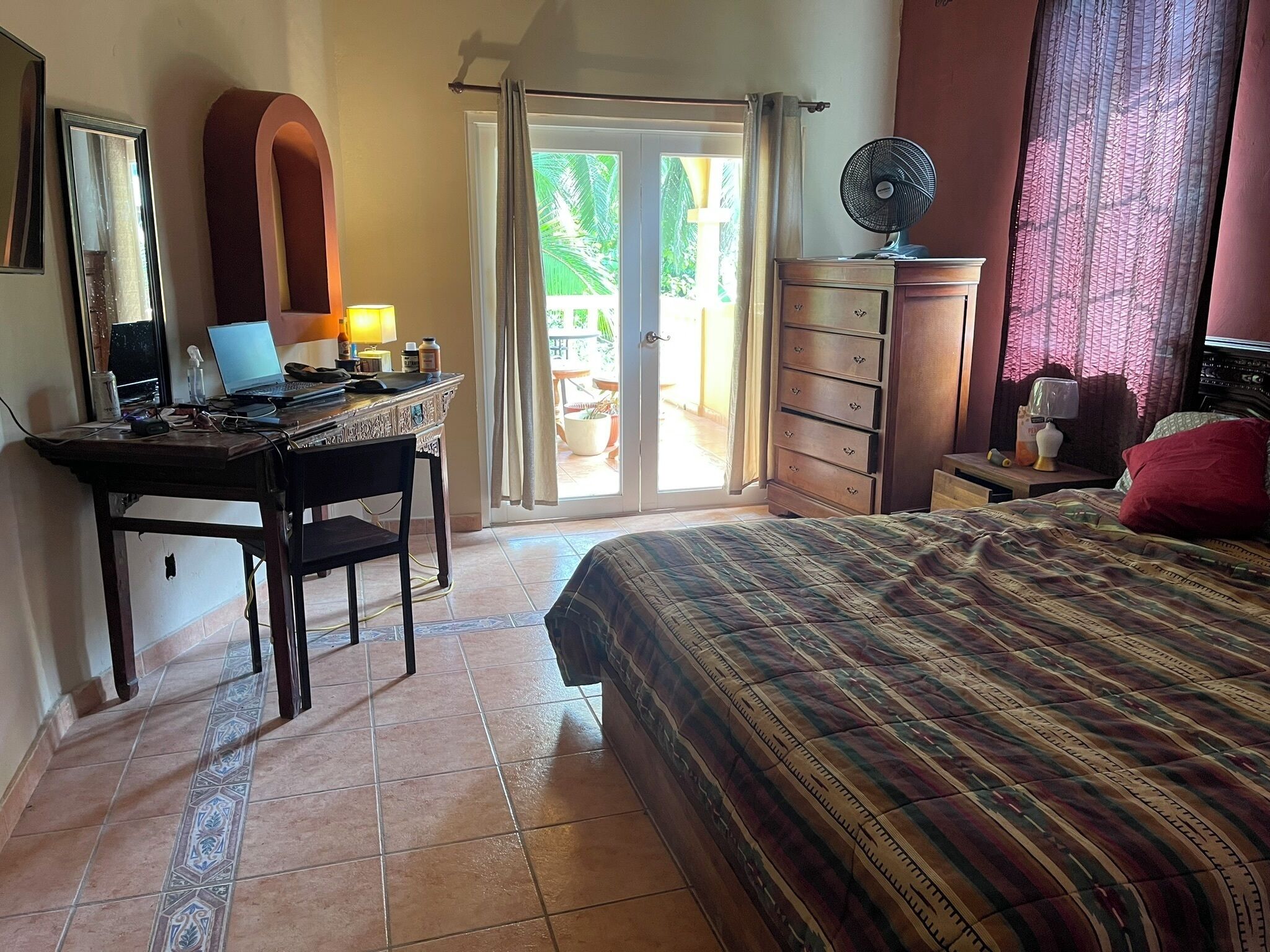 Ein Schlafzimmer mit einem Bett, einem Schreibtisch mit Laptop, einer Kommode und einem Fenster mit Vorhängen.