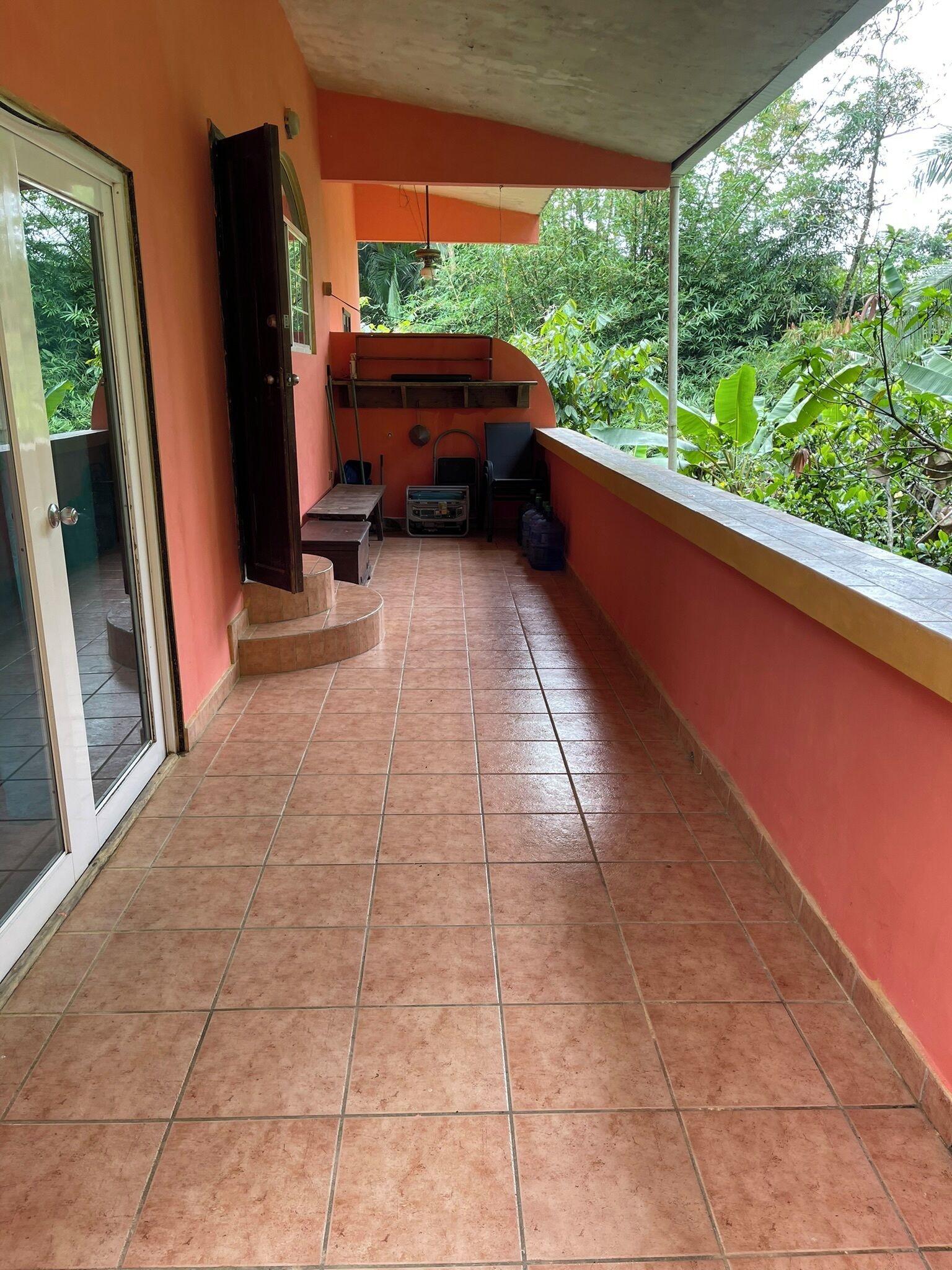 Un balcón cubierto con piso de baldosas, un pequeño espacio de descanso y vista a follaje.