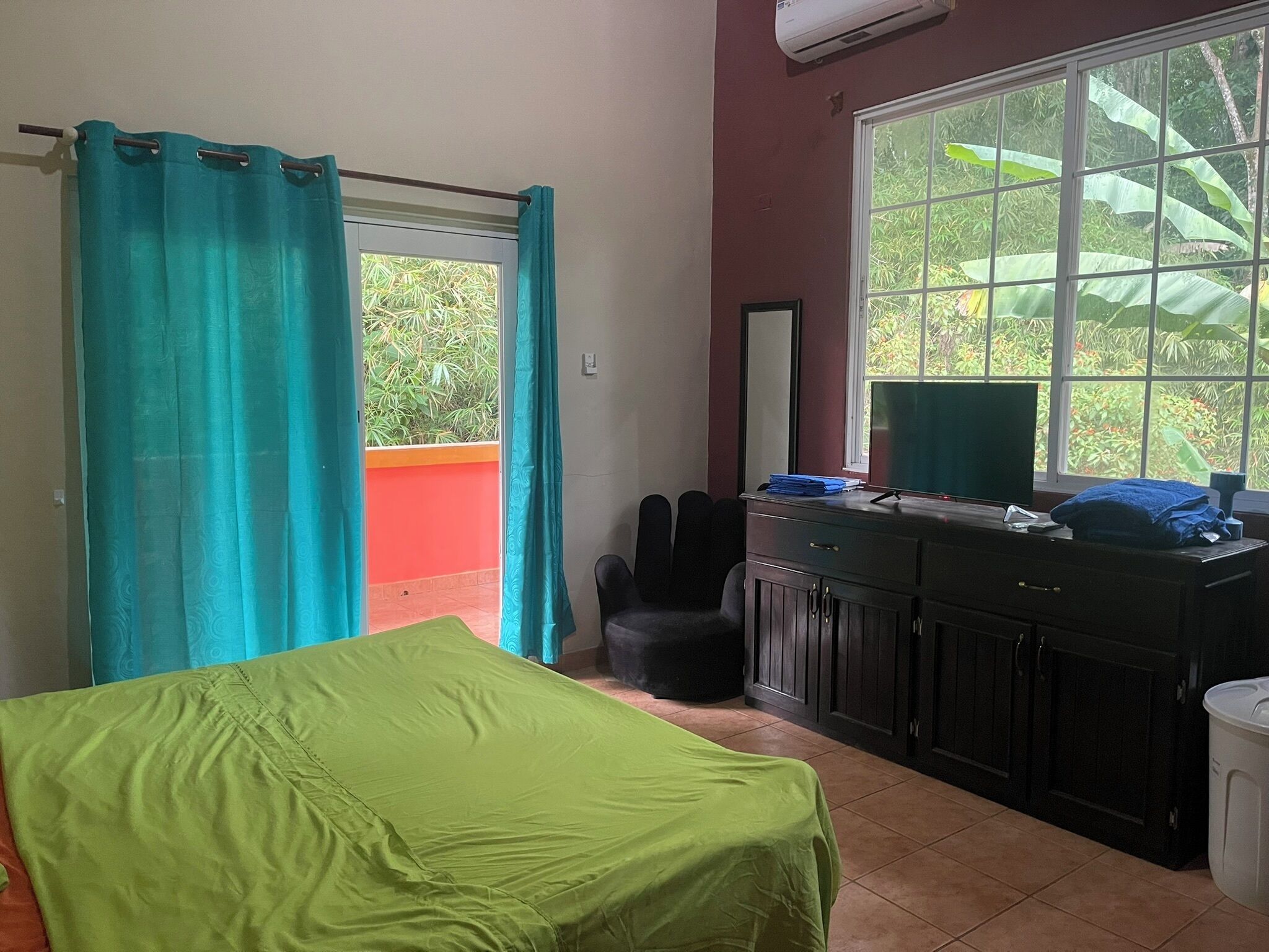 Ein Zimmer mit Bett, Schreibtisch mit Computer, Stuhl und Fenster mit Blick auf Grünflächen.