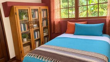 Un dormitorio con una cama, una estantería de madera y un ventanal con vistas a zonas verdes.