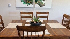 Une table à manger agrémentée d’un centre de table noir, entourée de chaises en bois, le tout placé devant un mur orné de deux tableaux abstraits.