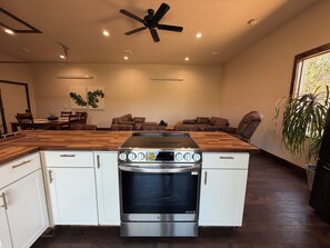 A modern kitchen with a built-in oven and stovetop, wooden countertops, white cabinetry, and a ceiling fan.