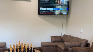 Un salon avec un téléviseur à écran plat fixé au mur, un jeu d’échecs posé sur une table basse et des canapés en cuir marron.