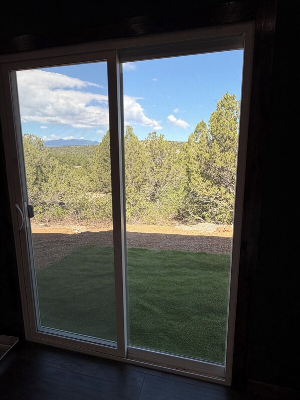 A view through a sliding glass door of a grassy yard with trees and a clear sky. - Private Retreat with Mountain Views with Full Kitchen & Peaceful Setting (Pueblo)