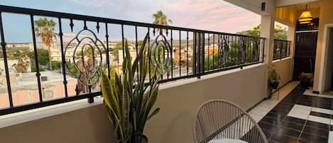 A balcony with two wicker chairs and a small table, a potted plant, and a view of the cityscape.