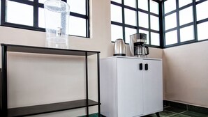 Un coin de pièce avec un meuble blanc, une étagère en métal noir et une machine à café posée sur le dessus du meuble.