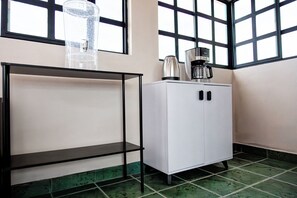 A corner of a room with a white cabinet, a black metal shelf, and a coffee maker on top of the cabinet.