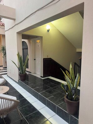 A hallway with a tiled floor, a staircase, and potted plants.