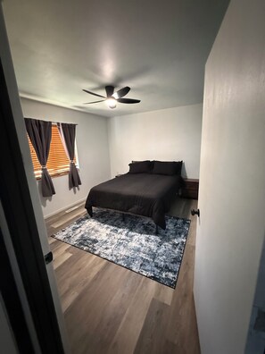 A bedroom with a bed, a ceiling fan, a window with curtains, and a wooden floor. - Fantastic 2-bedroom house with AC in friendly Spearfish (Spearfish)