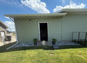 A single-story building with a flat roof, a visible door, and a small dog standing in the entrance. - Fantastic 2-bedroom house with AC in friendly Spearfish (Spearfish)