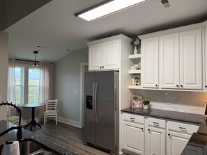 Eine moderne Küche mit weißen Schränken, einem Edelstahl-Kühlschrank, einem Essbereich mit Tisch und Stühlen sowie einem Ausblick durch das Fenster.