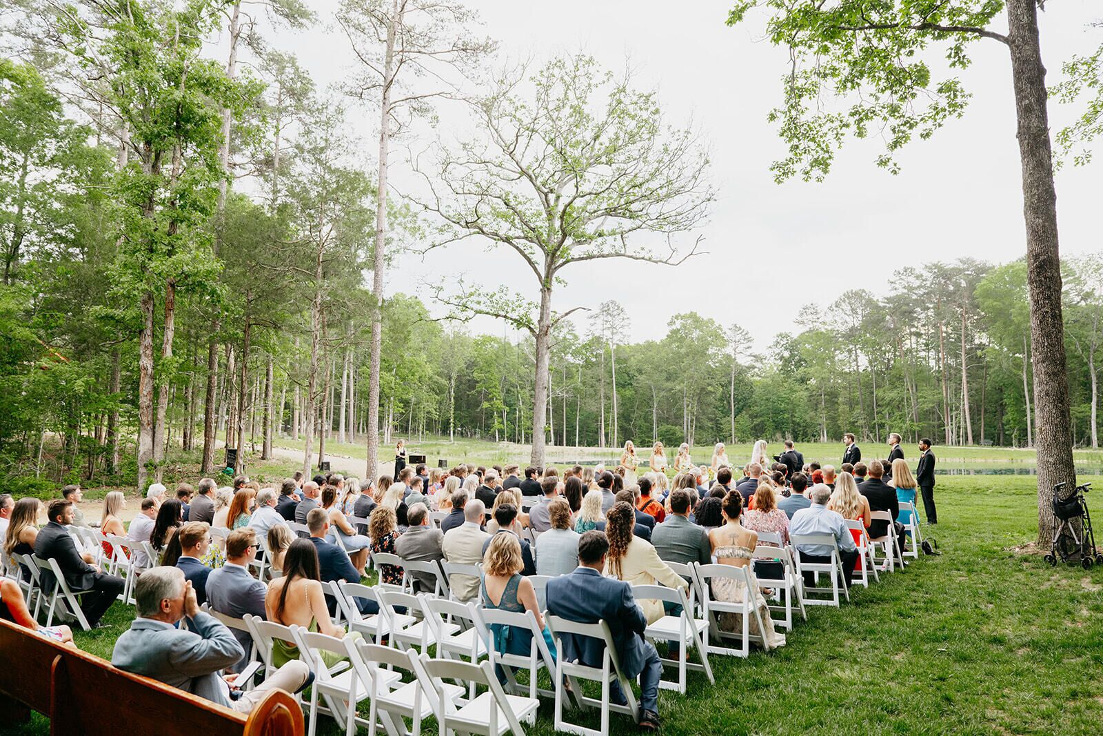 An outdoor event with attendees seated on white chairs facing a speaker.