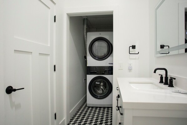 A laundry room with a washing machine and dryer, a sink with a faucet, and a door with a handle.