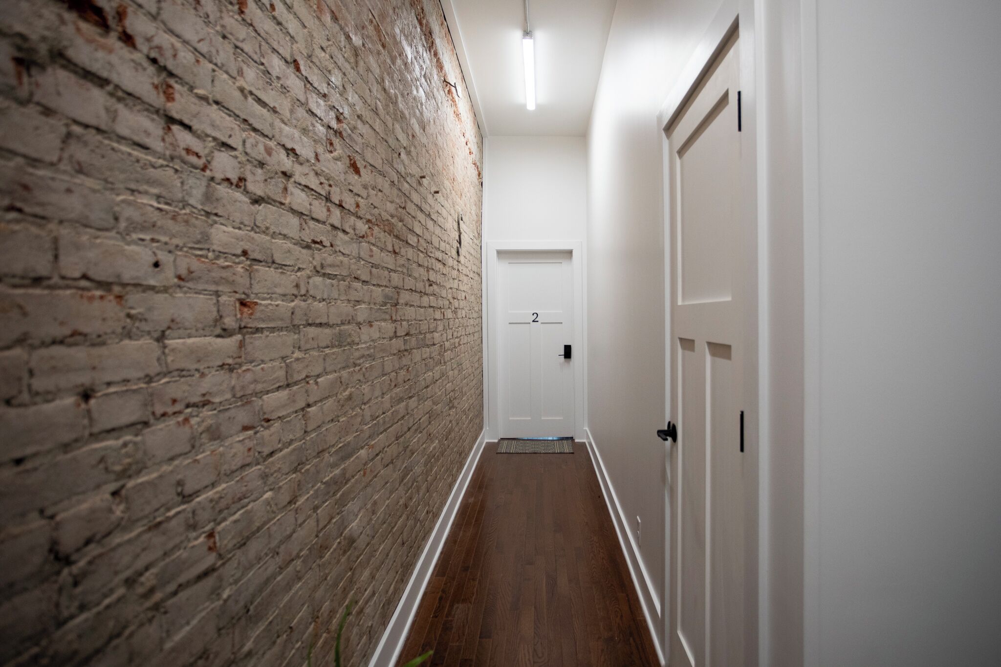A hallway with a brick wall on one side and white doors on the other.