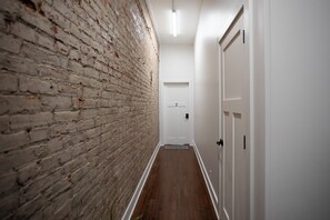 A hallway with a brick wall on one side and white doors on the other.