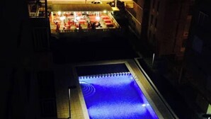 A swimming pool with a blue illuminated edge, surrounded by buildings. - Beachfront apartment with pool, parking & sea view, Gandia (Grau i Platja)