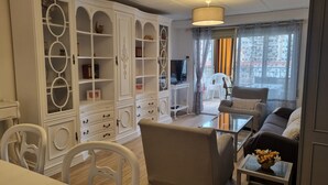A living room with a sofa, armchairs, a coffee table, and a TV. There is a large white cabinet with multiple shelves and drawers. - Beachfront apartment with pool, parking & sea view, Gandia (Grau i Platja)