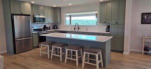 A kitchen with a central island, bar stools, a refrigerator, microwave, and a window with a view. - Luxury Lakeview Home with Panoramic Views. Sleeps 10 (Golden)