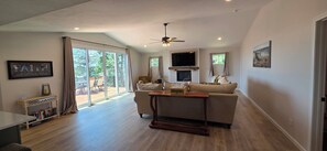 A spacious living room with a sofa, a coffee table, and a television. There is a balcony with a view of trees. - Luxury Lakeview Home with Panoramic Views. Sleeps 10 (Golden)