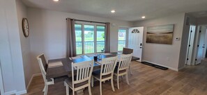 A dining area with a table and chairs, a clock on the wall, and a view of the outdoors through large windows. - Luxury Lakeview Home with Panoramic Views. Sleeps 10 (Golden)