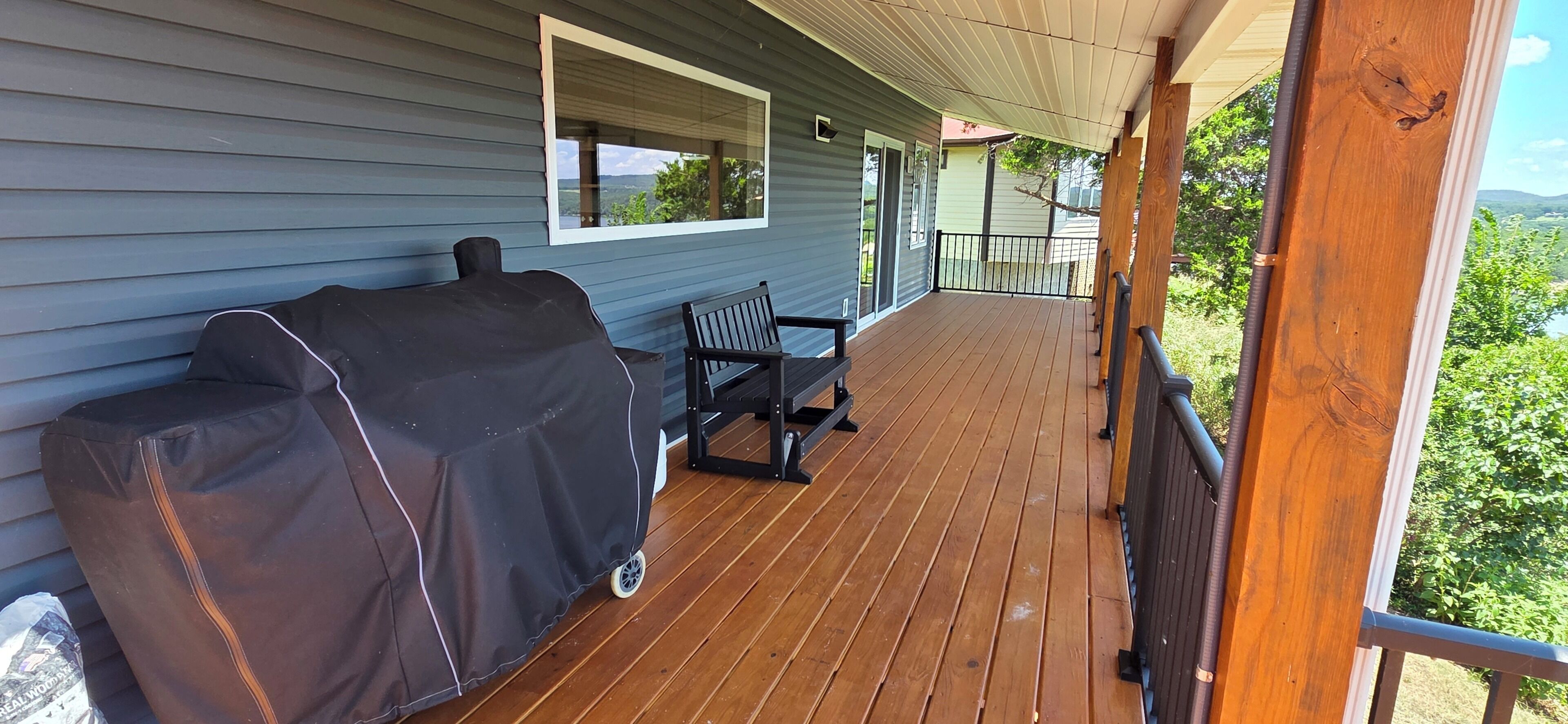 A covered wooden deck with a grill and a table.