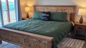 A bedroom with a wooden bed frame, green bedding, a ceiling fan, and a view of the outdoors through a window. - Luxury Lakeview Home with Panoramic Views. Sleeps 10 (Golden)