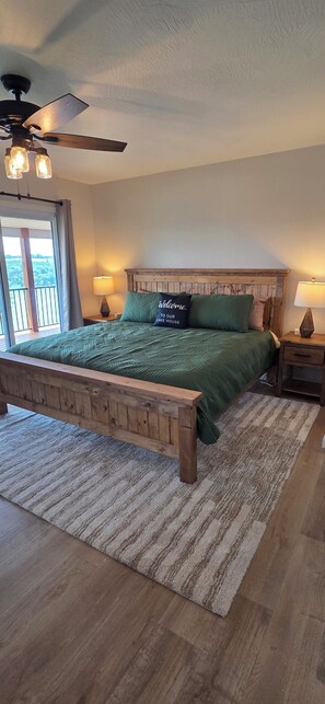 A bedroom with a wooden bed frame, green bedding, a ceiling fan, and a view of the outdoors through a window. - Luxury Lakeview Home with Panoramic Views. Sleeps 10 (Golden)