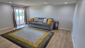A living room with a grey sofa, a patterned rug, and a view through a glass door. - Luxury Lakeview Home with Panoramic Views. Sleeps 10 (Golden)