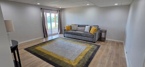 A living room with a grey sofa, a patterned rug, and a view through a glass door. - Luxury Lakeview Home with Panoramic Views. Sleeps 10 (Golden)