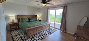 A bedroom with a wooden bed, two bedside lamps, a ceiling fan, and a view of the outdoors through a sliding glass door. - Luxury Lakeview Home with Panoramic Views. Sleeps 10 (Golden)