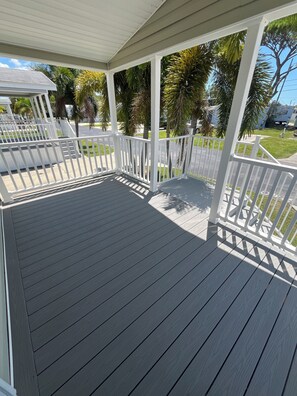 A covered wooden deck with white railings, surrounded by palm trees and a clear sky. - Snowbird Retreat in Beautiful Bradenton Florida! (Bradenton)