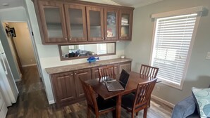Uma sala de jantar com mesa e cadeiras de madeira, uma cozinha com armários de madeira e uma janela com persianas.