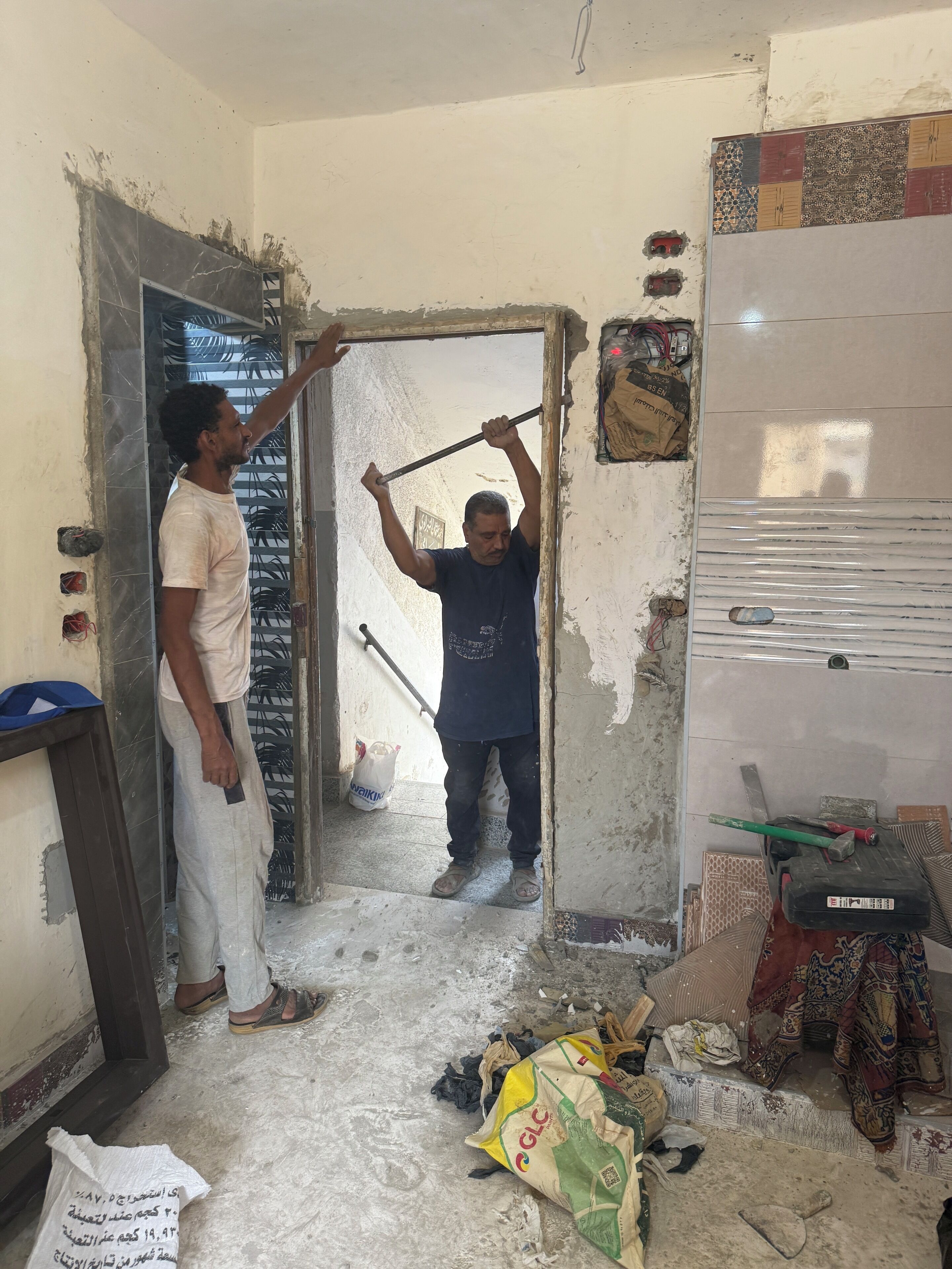 Een kamer in renovatie met zichtbare muren, een gedeeltelijk open deur en bouwmaterialen verspreid.