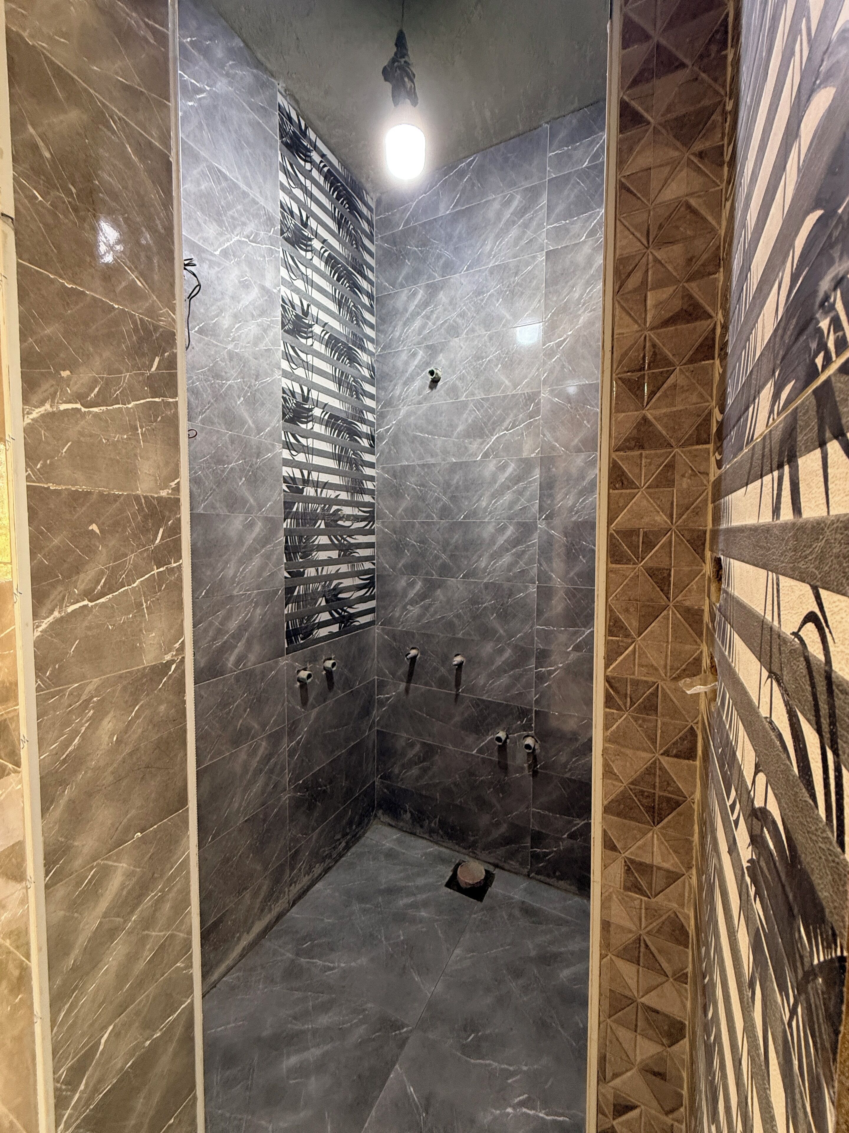 A modern bathroom with a shower area, marble walls, and a geometric patterned tile design.