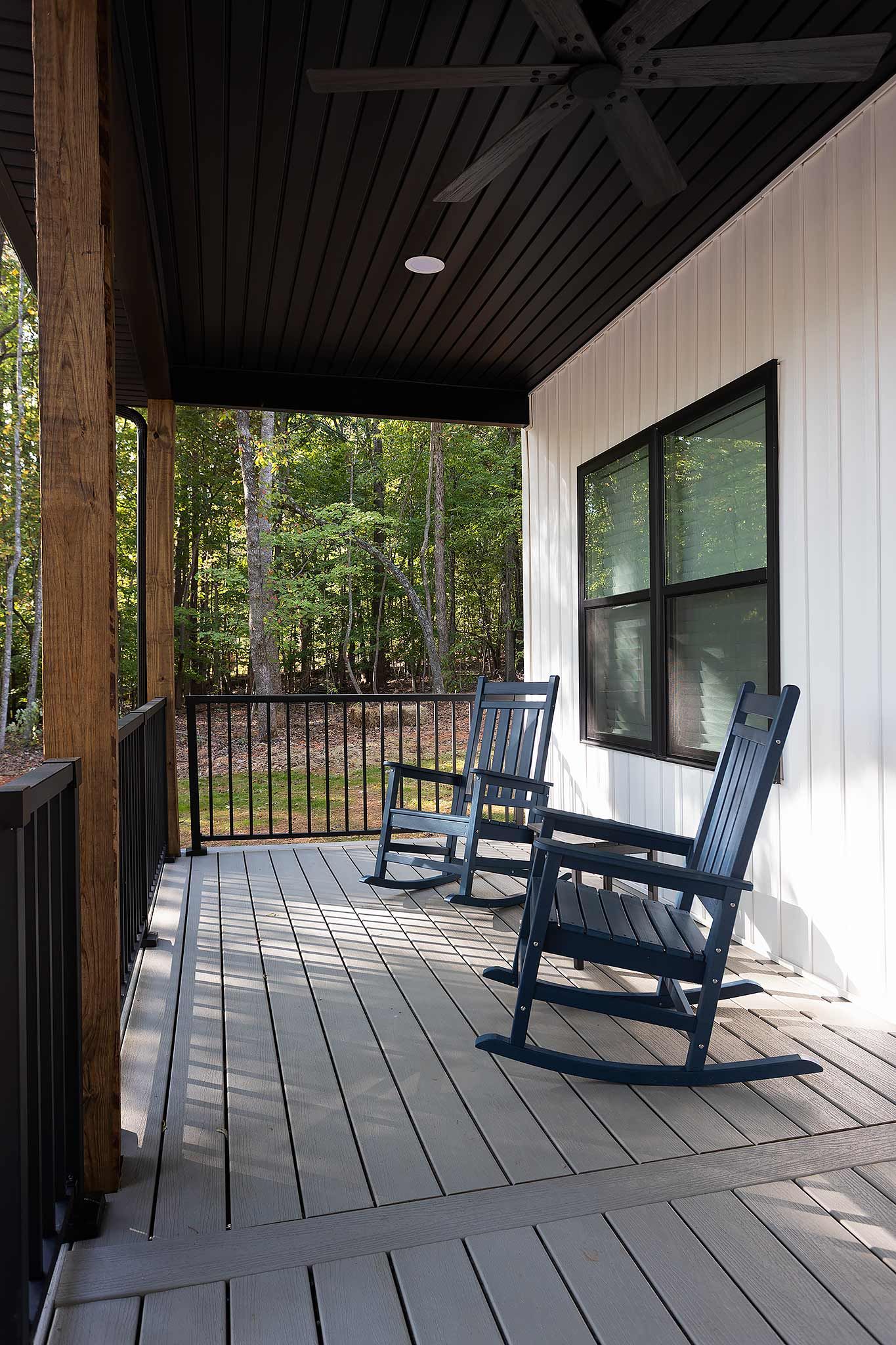 A covered porch with two rocking chairs and a window overlooking a wooded area.