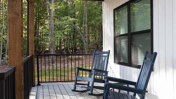 A covered porch with two rocking chairs and a window overlooking a wooded area.